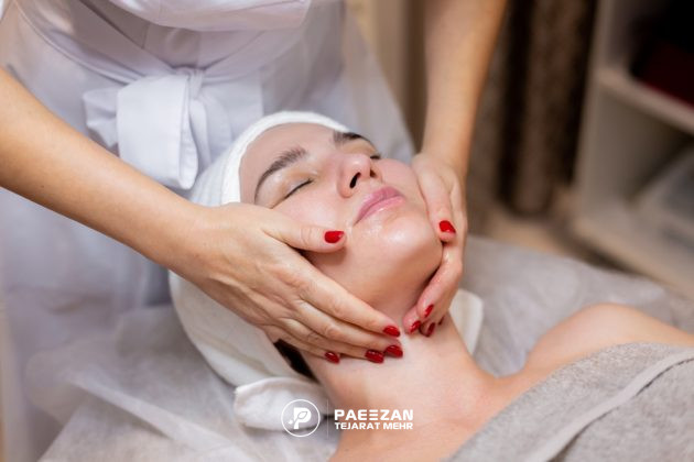 دختری که روی تخت ماساژ دراز کشیده و یک زن با دو دست صورت او را ماساژ می دهد