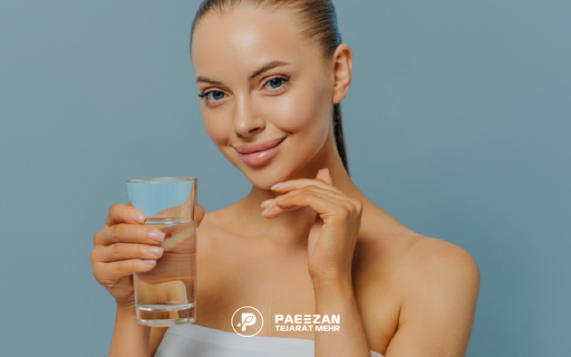 دختری که موهای خود را بسته و لبخند زده است و یک لیوان آب در دست گرفته است