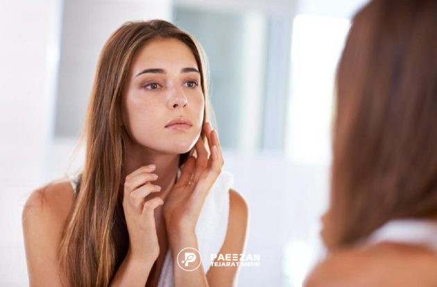 دختر جوان که خود را در آینه نگاه می کند و صورت خود را لمس می کند