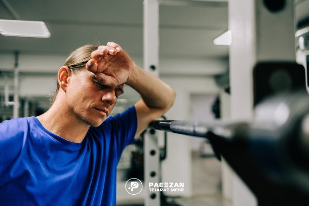 مردی که در باشگاه تمرین می کند و خسته شده است و دستش را روی پیشانی خود گرفته است