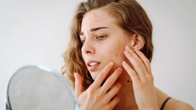 دختری که در آینه صورت خود را نگاه می کند
