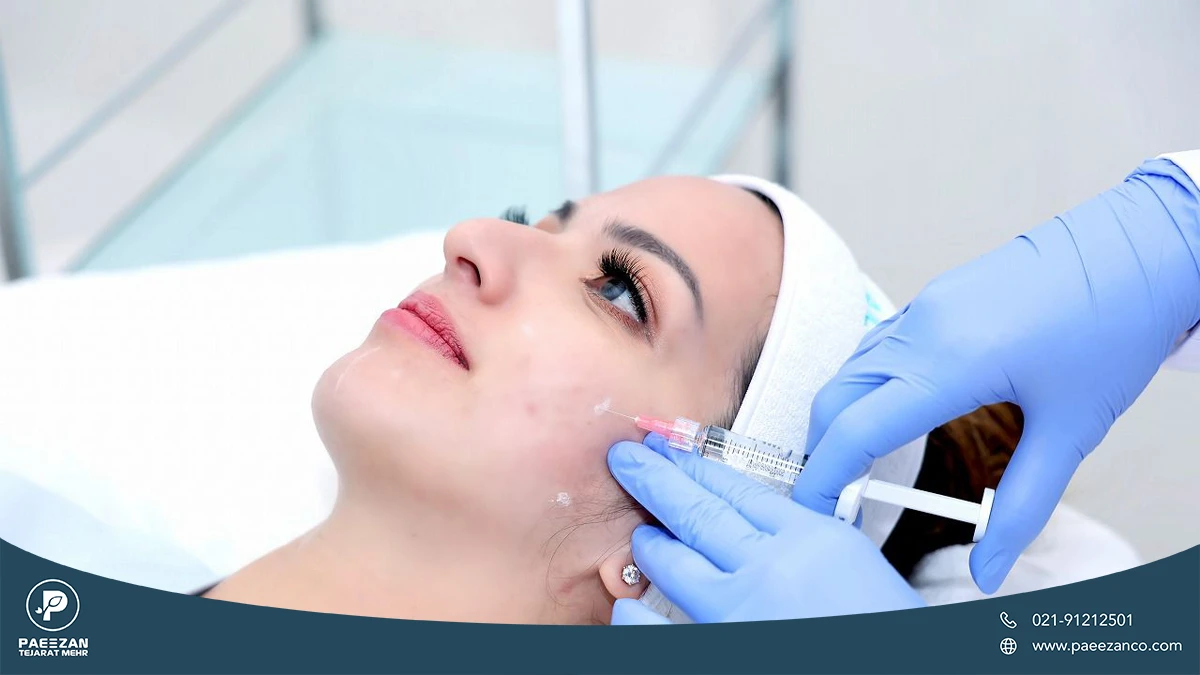 دختری که روی تخت کلینیک دراز کشیده و پزشک به بالای گونه او مزوژل تزریق می کند