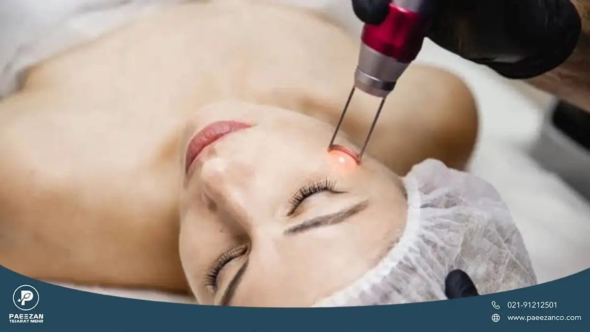 دختری که روی تخت کلینیک دراز کشیده و سر خود را به سمت چپ متمایل کرده و پزشک با دستگاه لیزر جوانساز صورت او را لیزر می کند